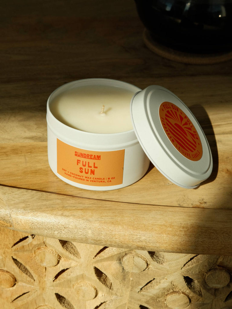 Candle in a white container with an orange label on a wooden surface