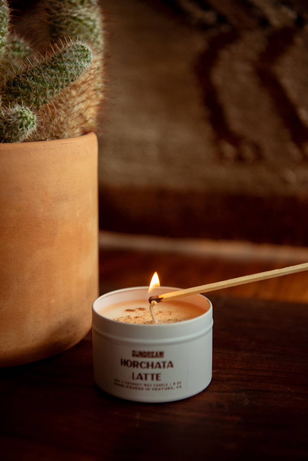 Candle labeled 'Horchata Latte' being lit with a match, next to a cactus plant.