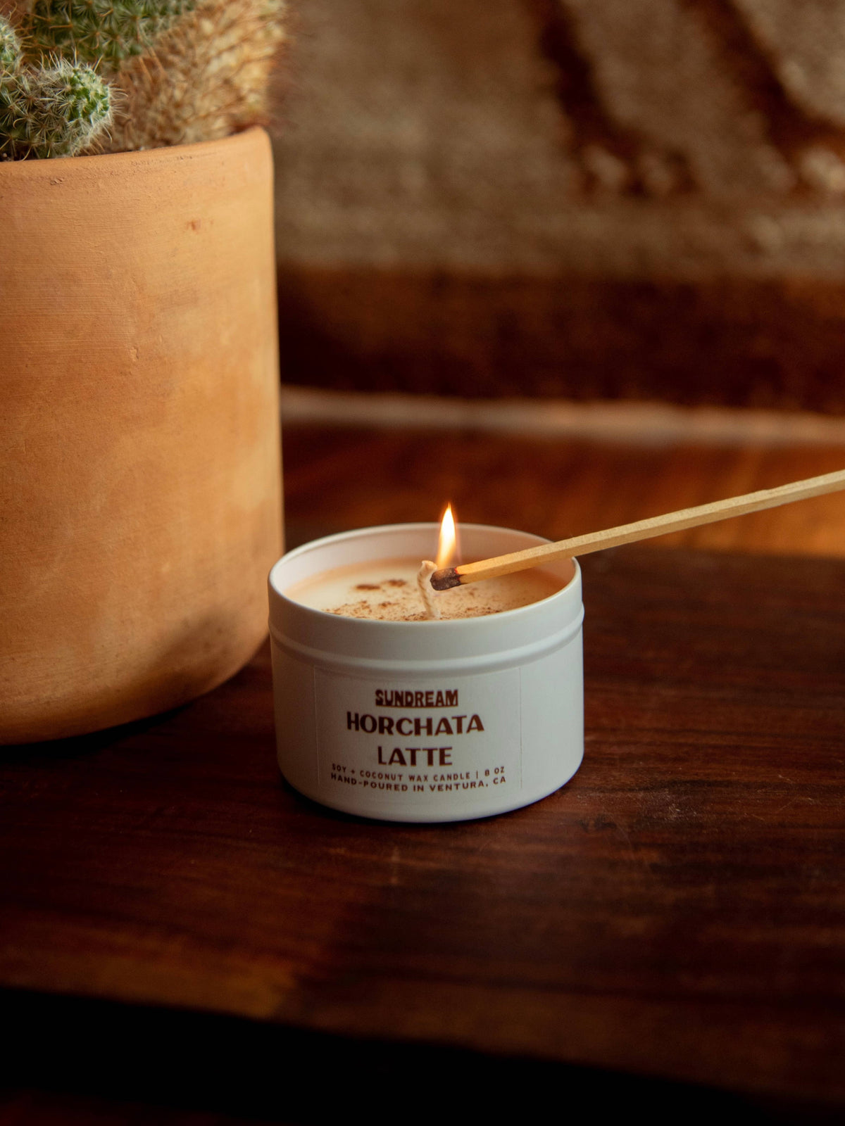 Candle labeled 'Horchata Latte' being lit with a match on a wooden surface.