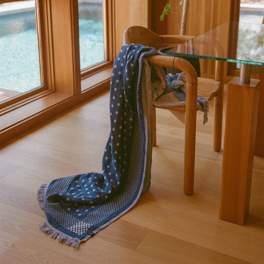 Blue patterned blanket draped over a wooden chair in a room with large windows.