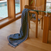 Blue patterned blanket draped over a wooden chair in a room with large windows.