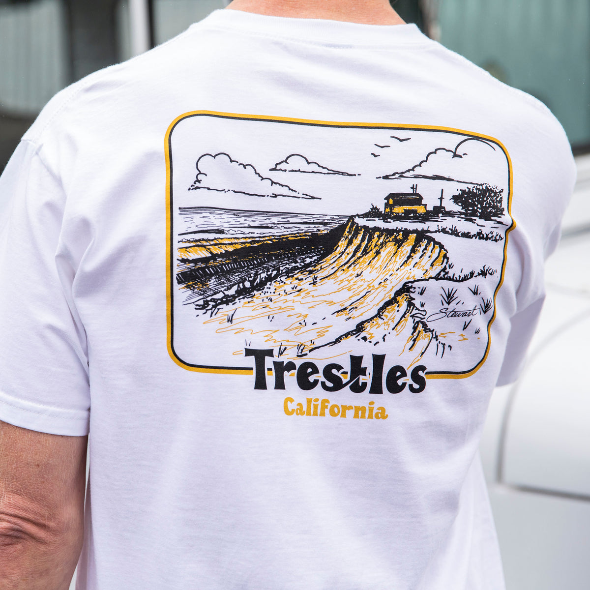 Surfer wearing the Stewart Trestles t-shirt in white, back view of shirt